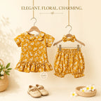A baby girl's two-piece outfit set featuring a short-sleeve top and matching bloomers, hanging on wooden hangers. The outfit is a mustard yellow color with a white floral print.