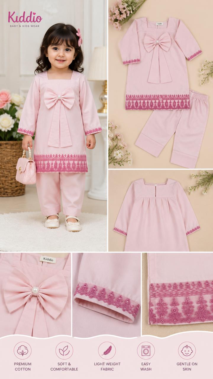 A children's two-piece pink outfit set with a matching top and pants, shown both on a model and as a flat lay. The set features a large bow on the chest, long sleeves, and a decorative pink patterned hem.