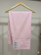 A pair of light pink lounge pants hanging from a wooden hanger against a neutral indoor wall. A white brand label reading 'kuddoo' is visible near the lower left hem.