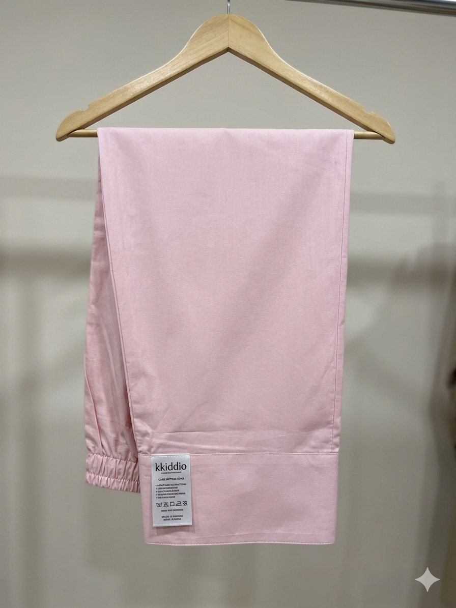 A pair of light pink lounge pants hanging from a wooden hanger against a neutral indoor wall. A white brand label reading 'kuddoo' is visible near the lower left hem.