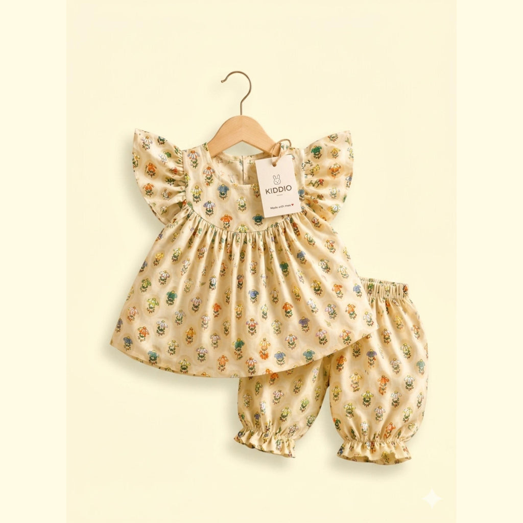 A baby girl's two-piece outfit set consisting of a flutter-sleeve dress and matching bloomers, hanging on a wooden hanger against a cream background. The outfit is beige with a colorful, small-scale woodland animal print.