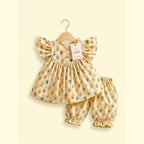 A baby girl's two-piece outfit set consisting of a flutter-sleeve dress and matching bloomers, hanging on a wooden hanger against a cream background. The outfit is beige with a colorful, small-scale woodland animal print.