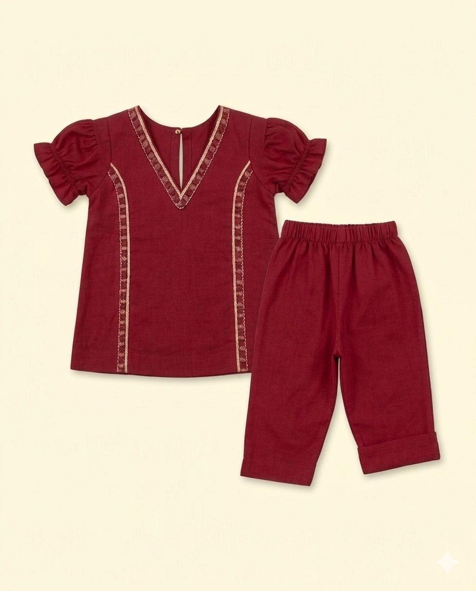 A two-piece children's outfit set in deep burgundy, featuring a short-sleeve top with puff sleeves and vertical embroidered trim, paired with matching elastic-waist pants, displayed on a solid cream background.