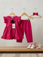 Pink children's outfit with top and pants on hangers, accompanied by baby shoes and toys on a shelf.