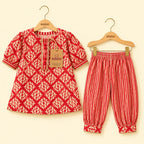 A two-piece children's outfit set by Kiddio, featuring a red and beige leaf-patterned short-sleeve top on a wooden hanger and matching red and beige vertically striped pants on a second hanger, displayed against a light cream background.