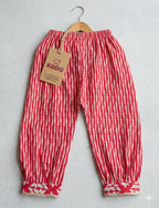 Red and white vertically striped cotton pants for toddlers, hanging on a wooden hanger with a brown paper brand tag that reads 'KIDDIO'.