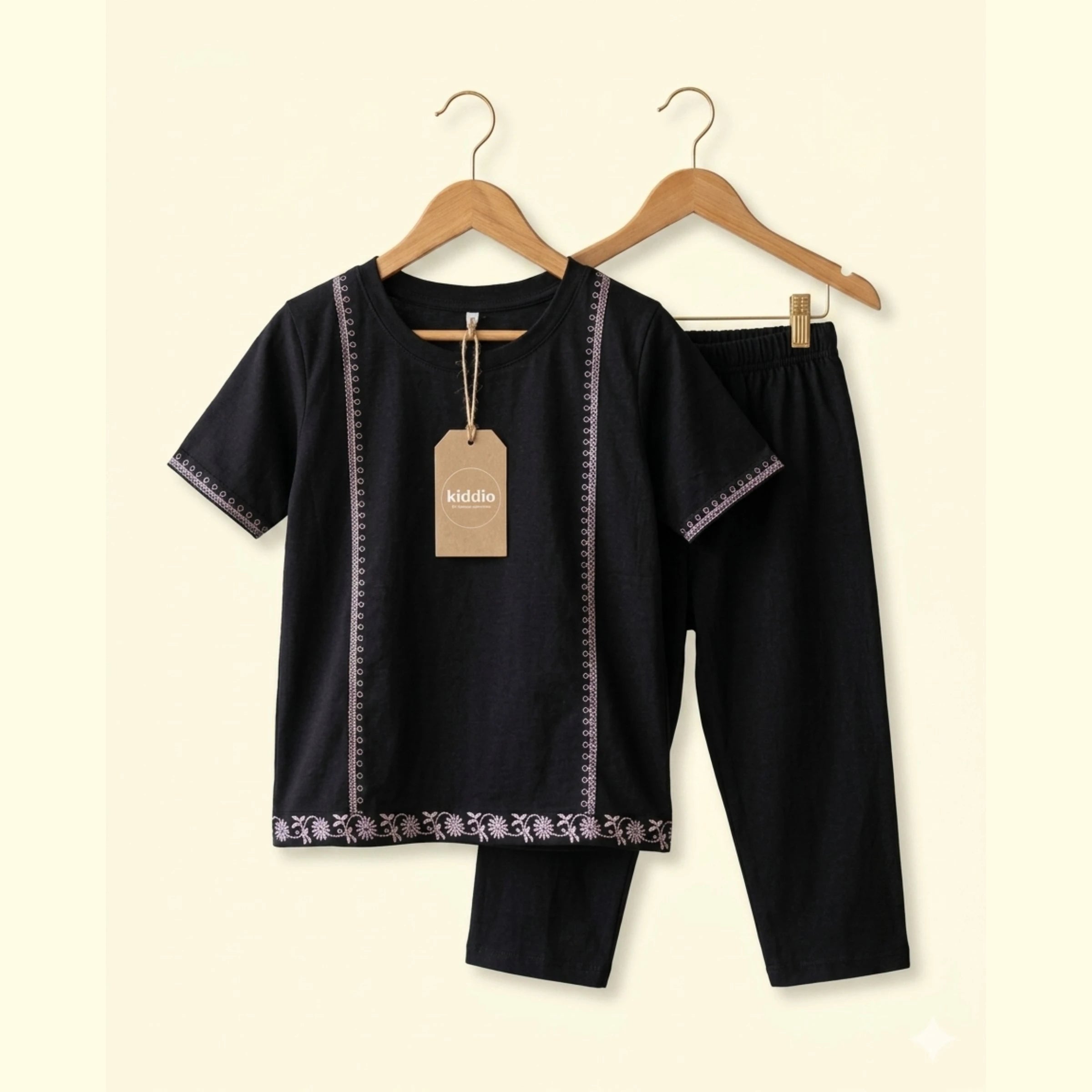 A two-piece kids' clothing set . The set is black with decorative purple and white floral lace trim along the neckline, sleeve cuffs, and hem.