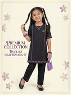 A young girl with braided pigtails models a black kurta and trouser set with purple embroidered borders. She is holding a small purple beaded handbag against a cream-colored background decorated with purple floral motifs and the text 'PREMIUM COLLECTION.