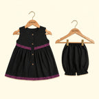 A toddler girl's two-piece outfit set consisting of a sleeveless black dress and matching bloomers, both hanging on wooden KIDDIO hangers against a light cream background.