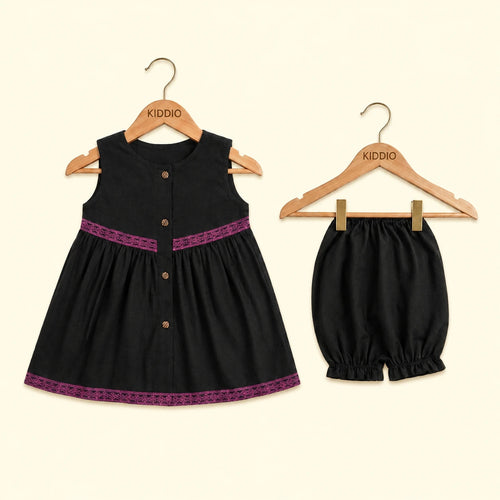 A toddler girl's two-piece outfit set consisting of a sleeveless black dress and matching bloomers, both hanging on wooden KIDDIO hangers against a light cream background.