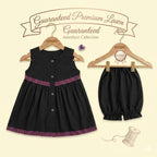 A two-piece baby outfit set from Kiddio, featuring a sleeveless black dress with purple patterned trim and button details, and matching black bloomers, displayed on wooden hangers against a light cream background with decorative text and illustrations.