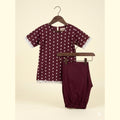 A two-piece baby outfit set consisting of a short-sleeve tunic top and matching pants, displayed on wooden hangers against a light beige background. The set is burgundy with white polka dots and white lace trim.