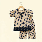 A two-piece baby clothing set consisting of a short-sleeve top and matching pants, displayed on a wooden hanger against a solid cream background. The set features a beige base with a navy blue floral pattern and solid navy blue lace trim details.