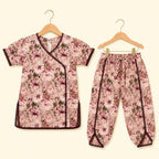 A two-piece children's outfit set consisting of a short-sleeve wrap-style top and matching pants, both featuring a pink and brown floral print with dark brown trim, displayed on wooden hangers against a light cream background.